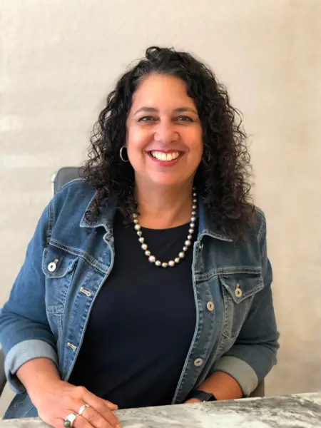 Smiling woman in a denim jacket and pearl necklace.